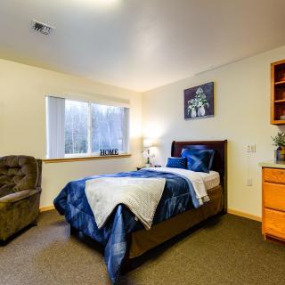 A cozy bedroom with a comfortable bed, armchair, and a window letting in natural light.