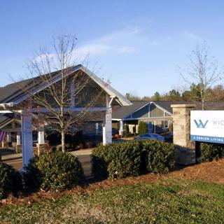 A building with a prominent sign in front, surrounded by shrubbery under a clear blue sky.