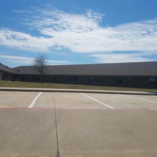 A clear day with a building in the background and a spacious parking lot.