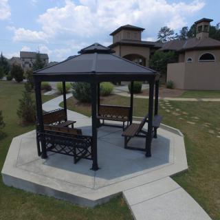 A gazebo with benches in a landscaped outdoor setting, surrounded by pathways.