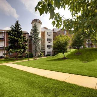 A sunny day view of an apartment complex with a unique silo feature and lush green surroundings.