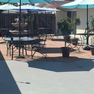 An outdoor patio area with tables, chairs, and umbrellas, featuring a central fountain and potted plants.