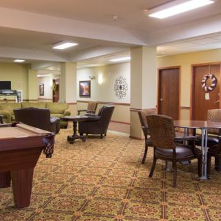 A cozy lounge area featuring a pool table, chairs, and tables on a patterned carpet.
