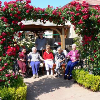 A group of people sitting in a garden surrounded by blooming roses.