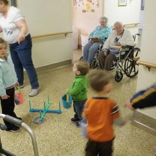 Children playing a game in a nursing home with elderly residents observing.
