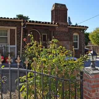 A charming brick house with a chimney, surrounded by a garden and iron fence.