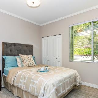A cozy and well-lit bedroom featuring a neatly made bed with decorative pillows, a window allowing natural light, and neutral-colored walls.