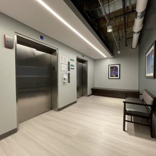 A modern corridor with elevators and a bench, featuring sleek interior design.