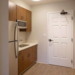 Compact kitchen in a modern apartment with wooden cabinetry, microwave, and refrigerator.