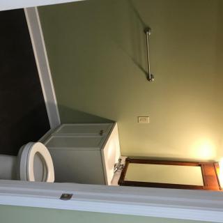 A small bathroom with a toilet, sink, mirror, and towel rack under warm lighting.