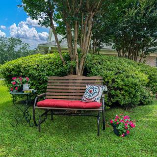 A cozy garden bench with a red cushion and decorative pillow surrounded by lush greenery and colorful flowers.