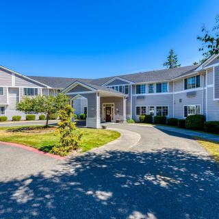 A sunny view of a large residential building with a driveway and landscaped surroundings.