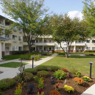 A well-maintained apartment complex with a landscaped courtyard featuring trees and flower beds.