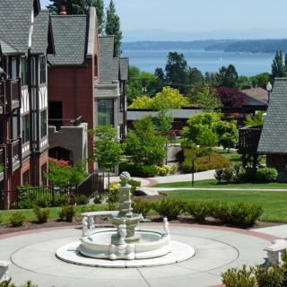 A scenic neighborhood with a central fountain, surrounded by houses and greenery, overlooking a lake.