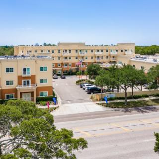 Aerial view of a residential apartment building with a parking lot and trees lining the street.