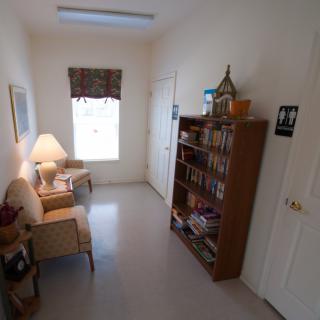A small waiting room with chairs, a bookshelf, and a window.
