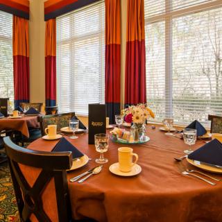 An elegantly set dining table in a restaurant with large windows and colorful curtains.