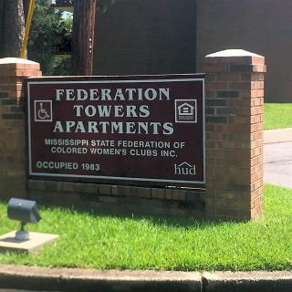 Sign for Federation Towers Apartments in a grassy area.
