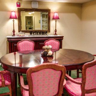 A cozy dining area featuring a round wooden table surrounded by pink upholstered chairs, complemented by a mirror and lamps on the sideboard.