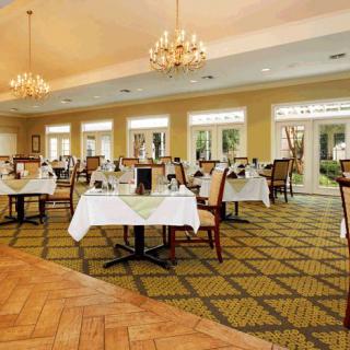An elegant restaurant dining room with tables set and chandeliers overhead.