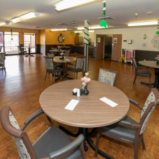 A spacious dining area with round tables and chairs, featuring wooden flooring and light decor.