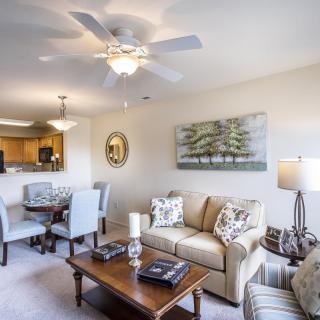 A cozy living room with a sofa, coffee table, dining area, and ceiling fan.