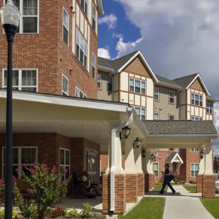 A multi-story residential building with brick exterior and covered walkways, set against a partly cloudy sky.