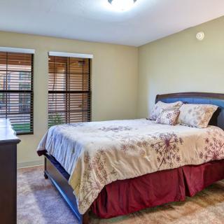 A cozy bedroom with a neatly made bed and natural light streaming through two windows.
