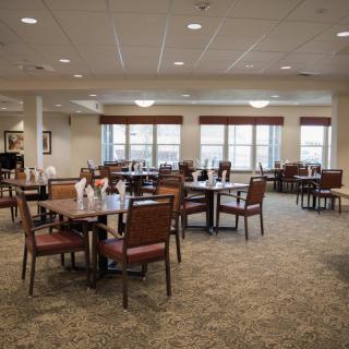 A spacious dining area with neatly arranged tables and chairs, illuminated by natural light from large windows.