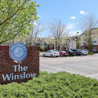A view of The Winslow, showcasing its entrance and parking area on a sunny day.