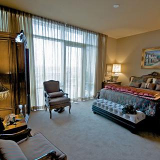 A luxurious bedroom featuring elegant furniture, a large bed with decorative pillows, and large windows with sheer curtains allowing natural light in.
