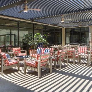 A stylish outdoor patio with colorful seating under a pergola casting striped shadows.