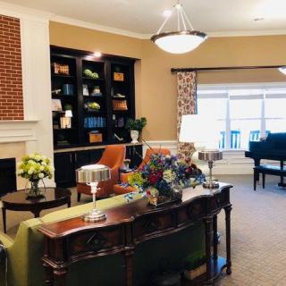 A cozy living room interior featuring a fireplace, bookshelf, and a piano with elegant furnishings.
