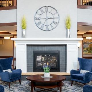 A modern living room with a fireplace surrounded by blue armchairs and a large wall clock.