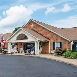 A welcoming residential building with a front porch, American flag, and lush landscaping against a clear sky.