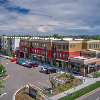 A modern shopping center with a parking lot and a cloudy sky backdrop.