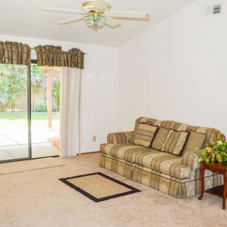 A cozy living room with a patterned sofa, ceiling fan, and sliding glass doors leading to an outdoor area.