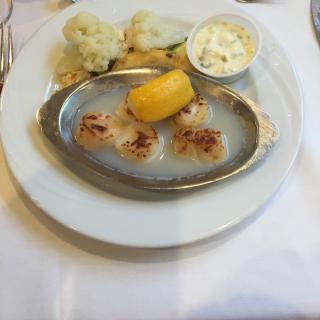 A plated meal featuring scallops with a lemon wedge, served alongside cauliflower and a small bowl of sauce.