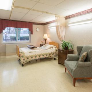 A well-lit hospital room featuring a single bed, a chair, and a window with curtains.