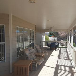 A covered porch with comfortable seating and a table, bathed in sunlight.