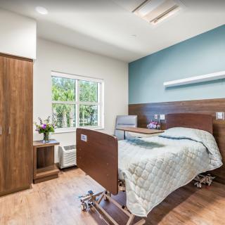 A clean and modern hospital room with a single bed, wooden furniture, and a large window.