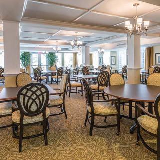 A spacious dining area with elegantly arranged tables and chairs under a chandelier.