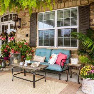 A cozy patio with a cushioned sofa, table, and vibrant plants.