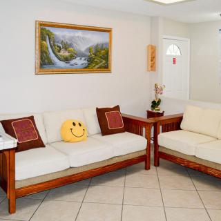 A cozy living room with two wooden sofas, a smiley face pillow, and a landscape painting on the wall.