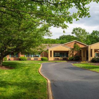A scenic view of a brick building surrounded by lush greenery and a winding driveway.