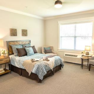 A cozy bedroom with a neatly made bed, bedside tables, lamps, and ambient lighting.