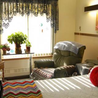 A cozy room with a reclining chair, bed, and plants by the sunlit window.