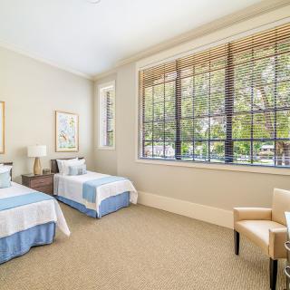 A bright bedroom featuring twin beds, large windows, and neutral-colored decor.