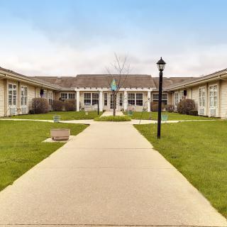 A serene courtyard featuring a well-maintained lawn and a central pathway leading to the building entrance, illuminated by a lamppost.