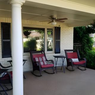 A cozy porch with red-cushioned chairs and a small table, perfect for relaxation.